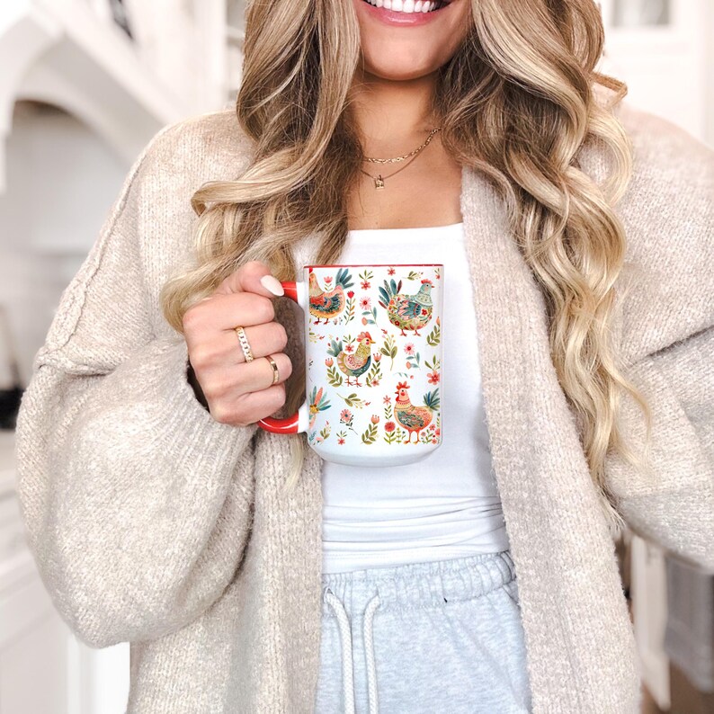 Puede incluir: Taza de cer&aacute;mica blanca con interior y asa rojos, con un dise&ntilde;o floral y de gallinas colorido. La taza la sostiene una persona. El dise&ntilde;o incluye varias gallinas, flores y follaje.
