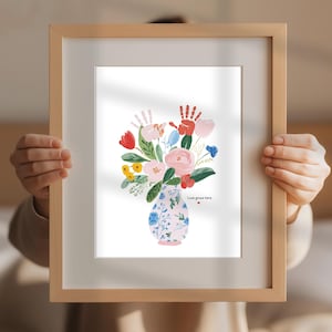 Op de afbeelding: Een ingelijste kunstdruk met een bloemenboeket in een decoratieve vaas. Het boeket bevat roze, rode, gele en blauwe bloemen met groene bladeren. De vaas is lichtroze met een blauw bloemmotief. De tekst "Love grows here" staat onderaan.