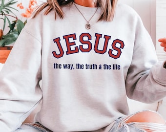 May include: A light gray sweatshirt with the word "JESUS" in red block letters with a navy blue outline. Below the word "JESUS" is the text "the way, the truth & the life" in navy blue.