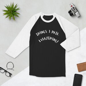 Puede incluir: Una camiseta de béisbol negra y blanca con un gráfico blanco que dice "Things I Hate: Everything!"