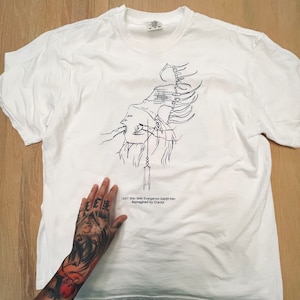 Può includere: Maglietta bianca con un disegno a linea nera di un personaggio dell'anime "Neon Genesis Evangelion". Il testo "1997 Shin Seiki Evangelion Gekijo-ban Reimagined by Crevis" è stampato sotto il disegno.