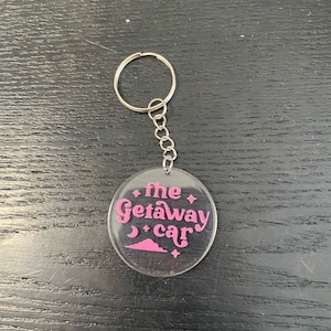 May include: A clear acrylic keychain with a pink design that says "the getaway car" with a crescent moon and stars.