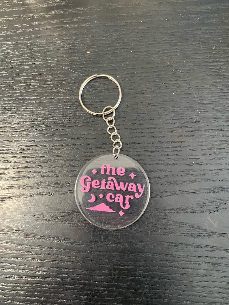 May include: A clear acrylic keychain with a pink design that says "the getaway car" with a crescent moon and stars.