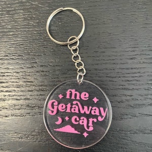 May include: A clear acrylic keychain with a pink design that says "the getaway car".