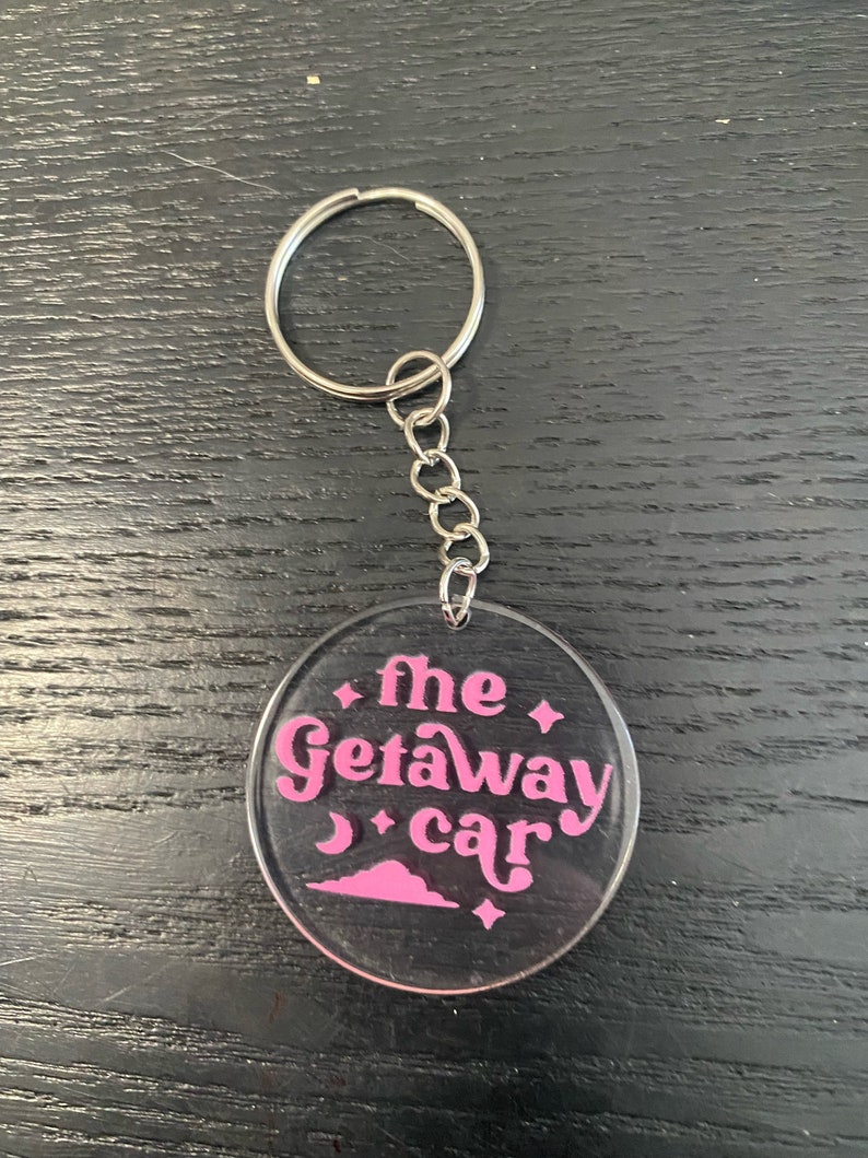 May include: A clear acrylic keychain with a pink design that says "the getaway car".