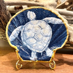 Decoupage and hand painted sea turtle on a gold trimmed flat scallop shell. 4 inch stand is an add’l order.