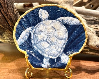 Decoupage and hand painted sea turtle on a gold trimmed flat scallop shell. 4 inch stand is an add’l order.