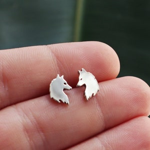 May include: A pair of silver wolf head stud earrings. The earrings are small and delicate, and they are perfect for adding a touch of whimsy to any outfit.