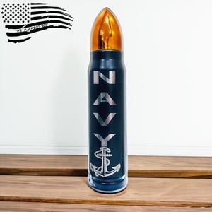 May include: A navy blue bullet-shaped water bottle with a gold-colored top. The word "NAVY" is vertically printed in silver, along with a silver anchor design. The American flag and "THE PATRIOT GUY" are in the upper left corner.