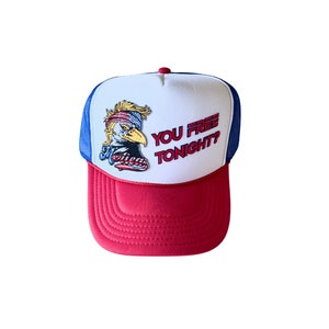 Op de afbeelding: Een witte en blauwe truckercap met een rode klep. De pet heeft een geborduurde Amerikaanse adelaar met de woorden "You Free Tonight?" in rood en blauw.