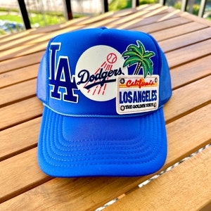 Può includere: Cappellino da baseball blu e bianco con logo dei Los Angeles Dodgers, una palma e una patch "California, Los Angeles, The Golden State".