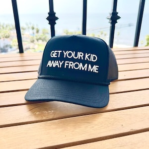 Peut inclure: Une casquette de camionneur noire avec un filet blanc à l'arrière. La casquette porte une inscription blanche qui dit "GET YOUR KID AWAY FROM ME".