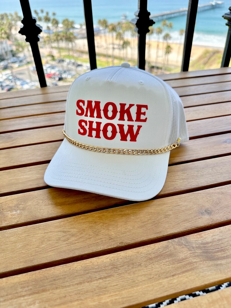 May include: White mesh trucker hat with a gold chain and red embroidered text that reads "SMOKE SHOW".