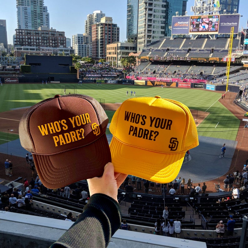 Puede incluir: Dos gorras de b&eacute;isbol con el texto "Who's Your Padre?" y el logotipo de los Padres de San Diego. Una gorra es marr&oacute;n y la otra es amarilla.