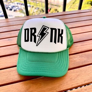 May include: A green and white trucker hat with a black lightning bolt and the word "DRNK" on the front.