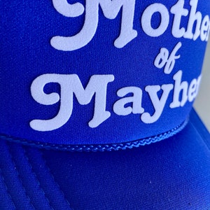 K&ouml;nnte beinhalten: Eine k&ouml;nigsblaue Trucker-Kappe mit wei&szlig; gesticktem Text, der "Mother of Mayhem" lautet.