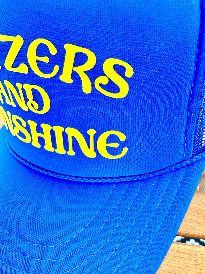 May include: Blue and yellow trucker hat with the text "Sizzlers and Sunshine" embroidered on the front.