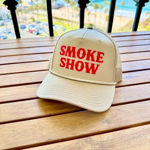 May include: A tan trucker hat with a red embroidered logo that says "SMOKE SHOW".