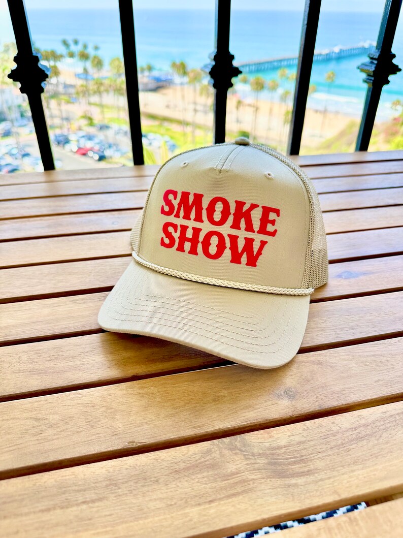 May include: A tan trucker hat with a red embroidered logo that says "SMOKE SHOW".