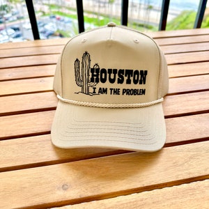 Może przedstawiać: Beżowa czapka trucker z czarnym kaktusem i haftowanym napisem "HOUSTON I AM THE PROBLEM" z przodu.