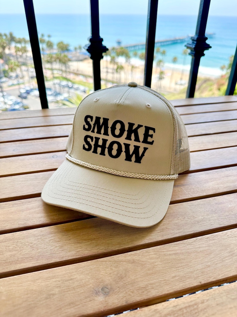 May include: A beige trucker hat with a black embroidered logo that says "SMOKE SHOW".