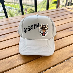Puede incluir: Una gorra de camionero de malla gris con una cara de tigre y las palabras "Go Get Em" bordadas en la parte delantera.