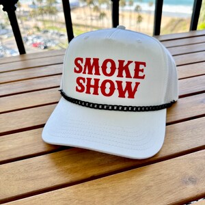 May include: White trucker hat with a black chain trim and red text that reads "SMOKE SHOW".