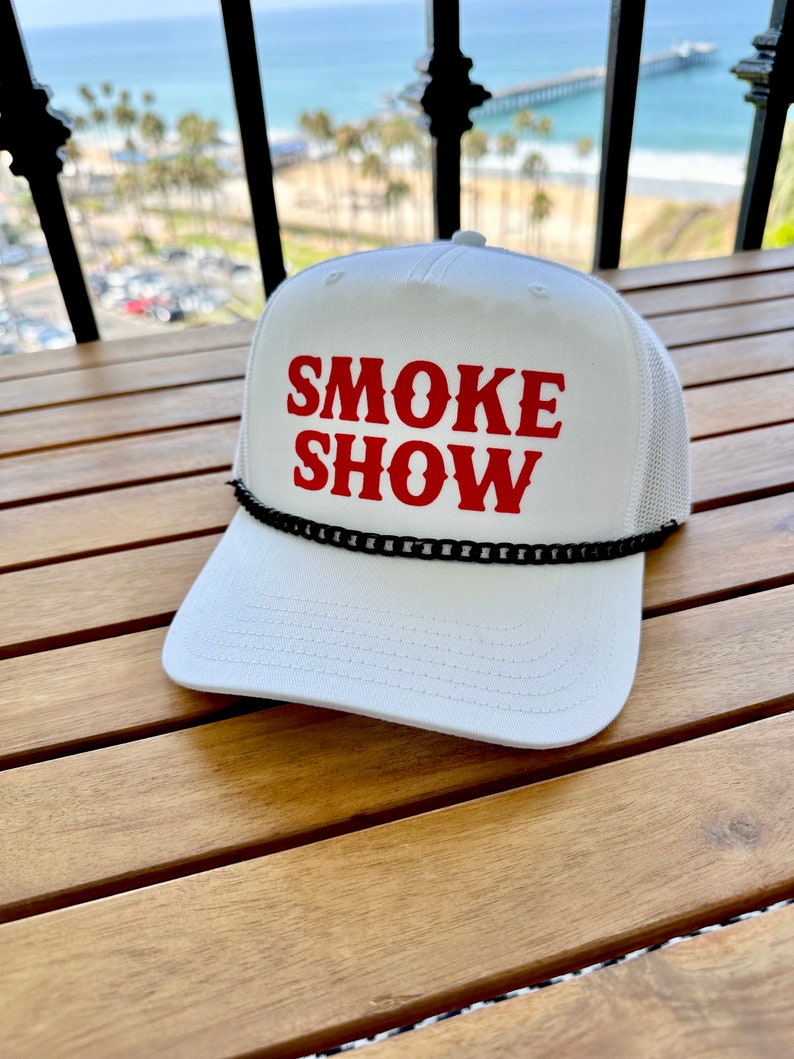 May include: White trucker hat with a black chain trim and red text that reads "SMOKE SHOW".