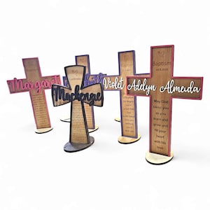 Puede incluir: Una colección de cruces de madera con nombres y fechas personalizados. Cada cruz presenta una combinación de colores única, con nombres en cursiva. Algunas cruces incluyen texto religioso. Diseñadas para bautizo o confirmación.