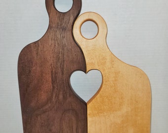 May include: Two wooden chopping boards, one dark brown and one light brown, are joined together to form a heart shape. The boards have a cutout heart shape in the centre.