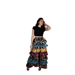 May include: A woman wearing a black crop top and a colourful, tiered maxi skirt with a high slit. The skirt has a variety of patterns and colours, including black, white, yellow, red, and blue.