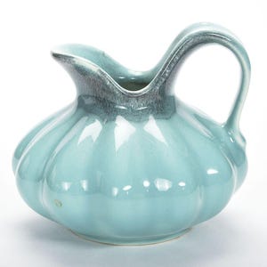 May include: A light blue ceramic pitcher with a rounded body and a flared spout. The pitcher has a textured, slightly rippled surface and a handle that curves up and over the top.
