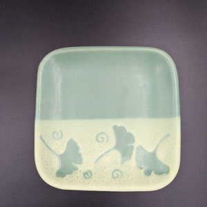 May include: A square ceramic dish with a light green glaze and a white bottom. The bottom has a design of ginkgo leaves in a light green color.