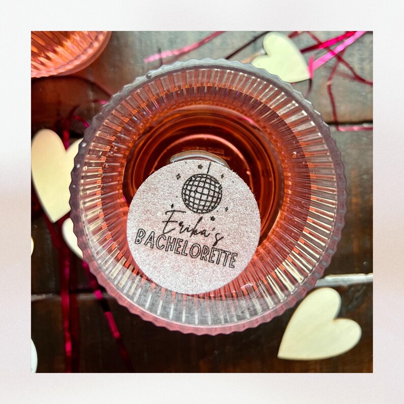 K&ouml;nnte beinhalten: Ein runder, silberner Glitzeraufkleber mit schwarzem Text, der "Erika's Bachelorette" lautet, und einer Discokugelgrafik.
