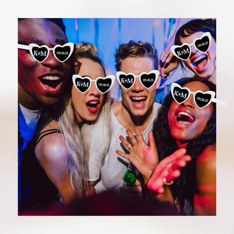May include: Four friends wearing white heart-shaped sunglasses with the text "K+M 09.30.25" printed on the lenses. The friends are smiling and looking at the camera.