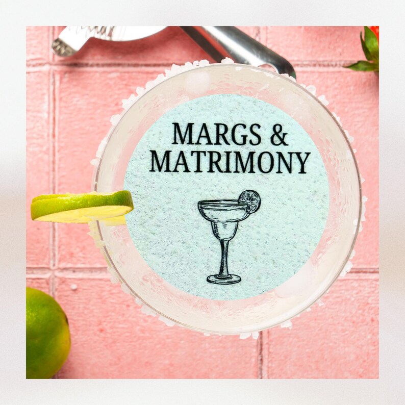 K&ouml;nnte beinhalten: Ein Margarita-Glas mit gesalzenem Rand, einem Limettenst&uuml;ck und einem blauen Hintergrund mit dem Text "MARGS & MATRIMONY".