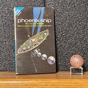 May include: A paperback science fiction novel titled "Phoenix Ship" by Walt and Leigh Richmond. The cover features a futuristic spaceship with a circular design and a dark blue background.
