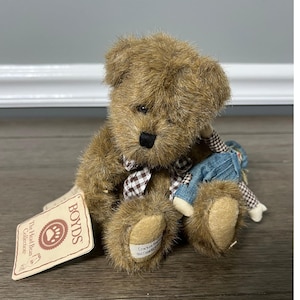 Pode incluir: Um urso de pelúcia marrom com um nariz preto e uma gravata borboleta xadrez. O urso está segurando uma pequena boneca usando macacão jeans. Uma etiqueta da "Boyds The Head Bean Collection" está anexada.