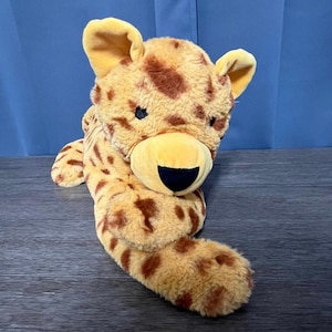 May include: A plush cheetah toy with brown spots on a yellow background. The toy is lying on its belly with its head turned to the side. It has a black nose and black eyes.