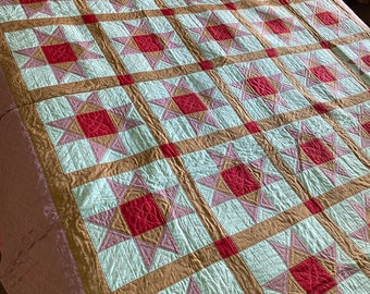 May include: A quilt with a pattern of stars in shades of red, pink, white, and brown. The quilt is made of fabric squares sewn together to create a geometric design.