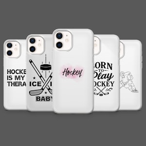 May include: A collection of five white phone cases with hockey-themed designs. The cases feature text like "Hockey is my therapy", hockey sticks, and the word "Hockey" in pink. The cases are for a smartphone.