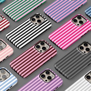 Könnte beinhalten: Eine Sammlung von Smartphone-Hüllen mit vertikalen Streifen in verschiedenen Farben wie Rot, Schwarz, Pink, Blau, Grün, Braun und Lila. Jede Hülle hat einen Ausschnitt für ein Dreifach-Kamerasystem und eine einheitliche rechteckige Form.