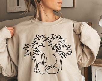 May include: Beige sweatshirt featuring a black graphic of Mickey Mouse standing in front of palm trees. The long-sleeved top has a crew neck and a relaxed fit, suitable for casual wear. The design is simple and clean, with a focus on the iconic character and tropical theme.