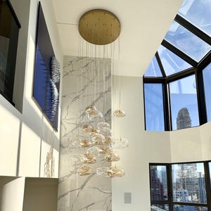 May include: A multi-pendant chandelier featuring numerous irregular, translucent amber-tinted glass globes suspended from a circular gold ceiling mount, arranged in a cascading cluster against a white marble fireplace surround.