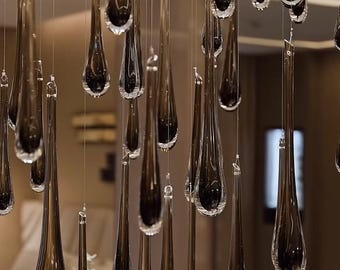 May include: A modern chandelier featuring numerous teardrop-shaped glass pendants. The pendants are a dark, smoky color and hang at varying lengths, creating a dynamic and elegant lighting fixture. The overall design is contemporary and sophisticated.