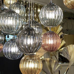May include: A collection of decorative glass globe pendant lights with ribbed textures in various colours, including clear, gold, and pink. The lights are hanging from a ceiling and are illuminated with warm white light bulbs.