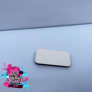Puede incluir: Un rectángulo blanco en blanco para sublimación con un borde negro. El espacio en blanco es una superficie lisa y sólida, ideal para la impresión personalizada. La imagen también incluye un logotipo de ERC Printing & Supplies.