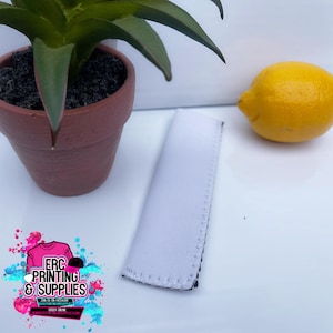 Puede incluir: Una funda blanca para bebidas con costuras negras, junto a una planta en maceta y un limón amarillo. La funda está en blanco y lista para personalizar. La imagen también incluye un logotipo de ERC Printing & Supplies.