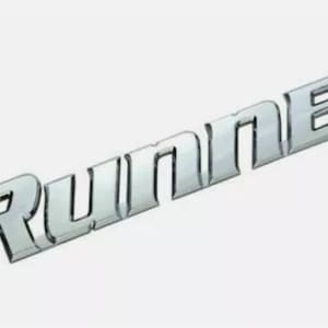 Puede incluir: Emblema cromado con el texto "4Runner" en una fuente estilizada. El emblema está ligeramente inclinado, con los números y letras en color plata metálico sobre un fondo blanco. El emblema es probablemente para un vehículo.