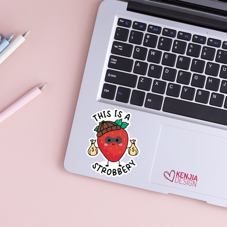May include: A red strawberry with a black eye mask and a brown hat is holding two bags of money. The text "This is a Strobbery" is written below the strawberry.